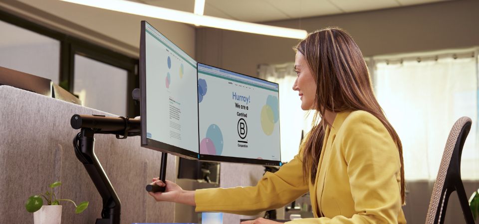 Vrouw stelt haar monitor in op de juiste hoogte met een ergonomische monitorarm voor een betere werkhouding en minder nekbelasting.